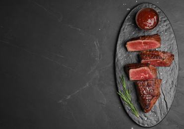 Photo of Delicious sliced beef tenderloin on black table, top view. Space for text