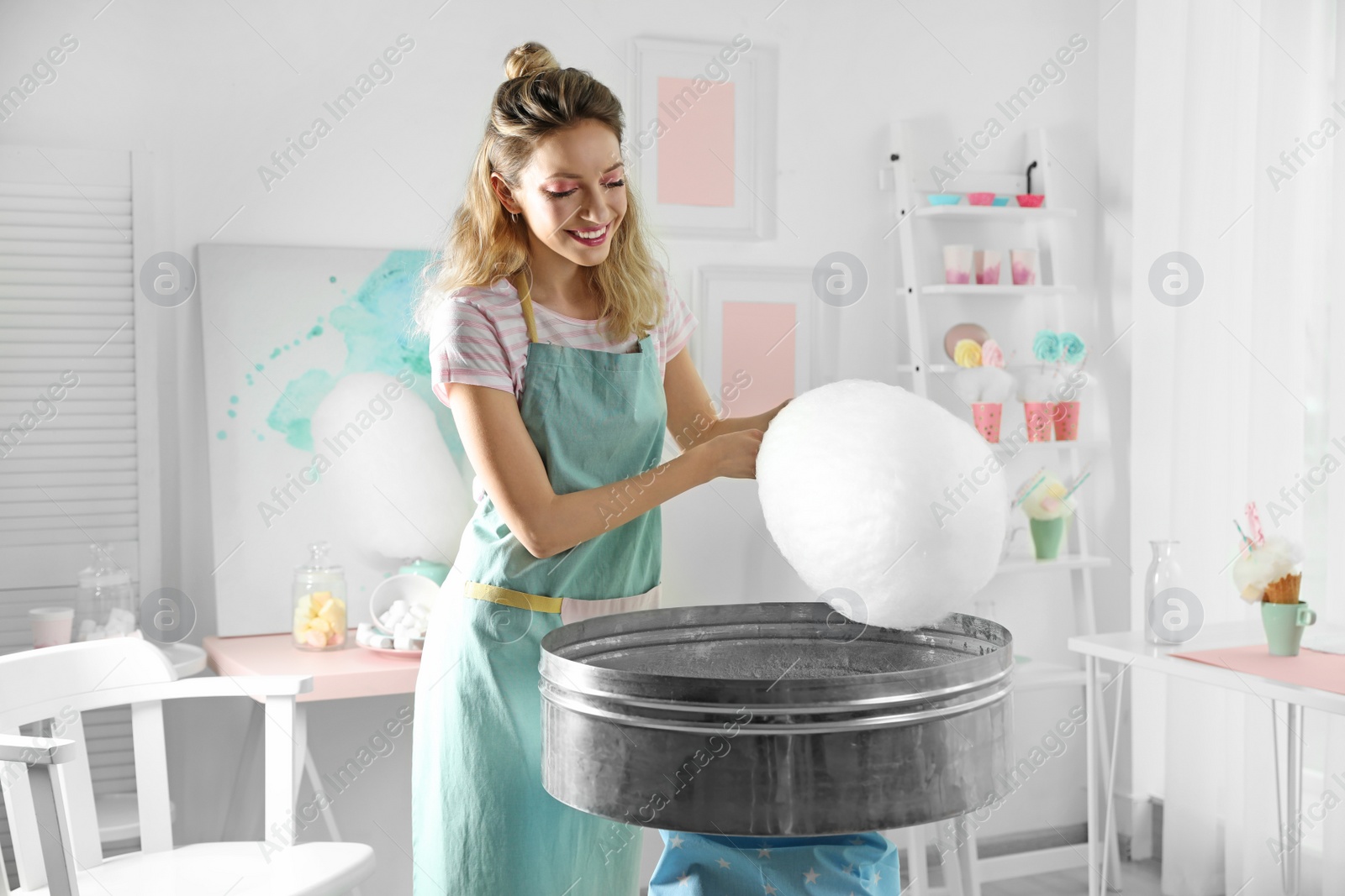 Photo of Young woman making cotton candy using modern machine in room