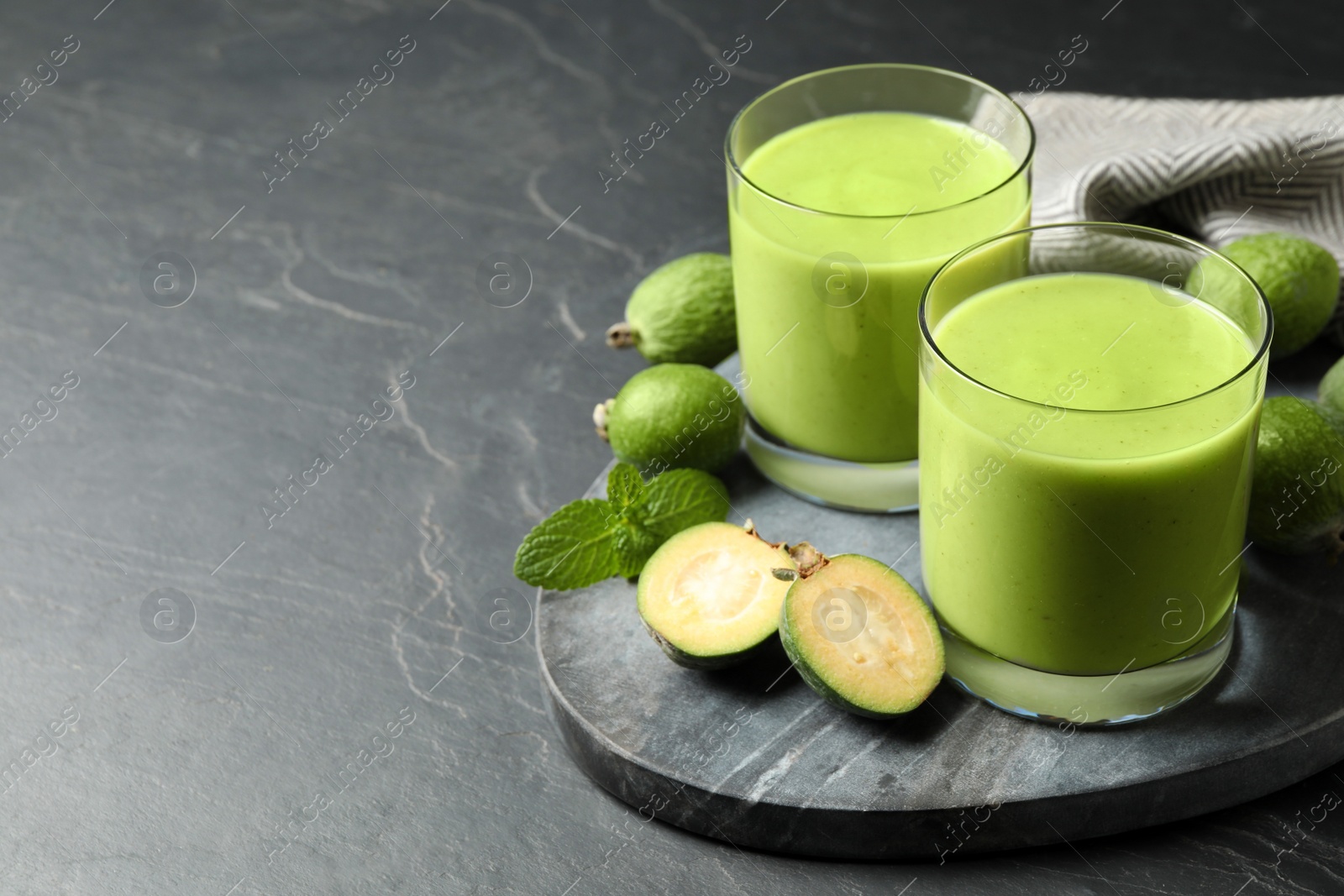 Photo of Fresh feijoa smoothie and fresh fruits on grey table, space for text