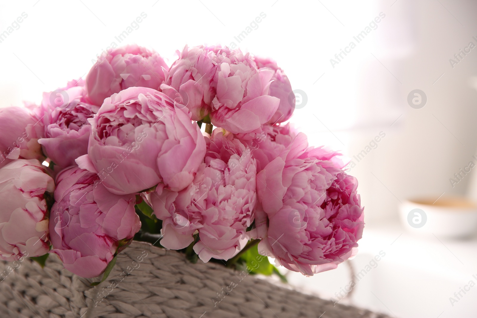 Photo of Basket with beautiful pink peonies in kitchen, closeup