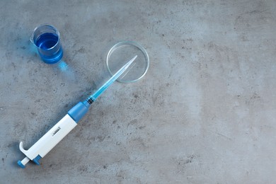 Photo of Laboratory analysis. Micropipette, petri dish and beaker on grey table, top view. Space for text