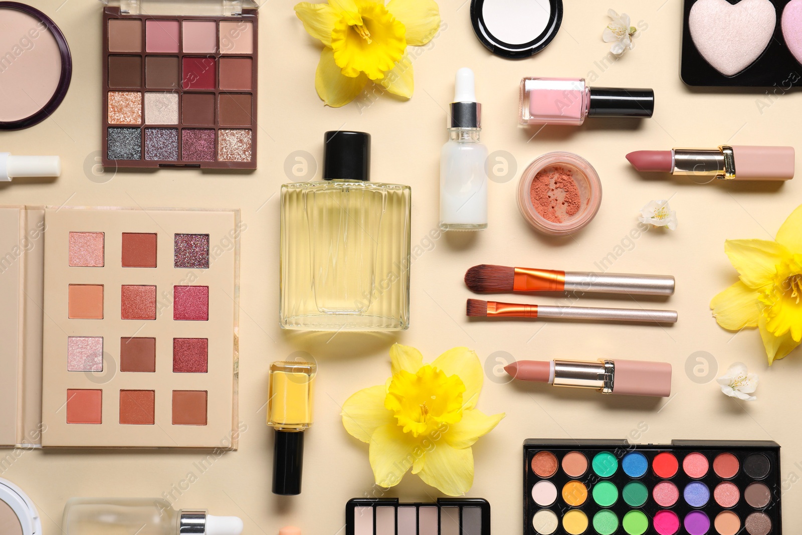 Photo of Flat lay composition with different makeup products and beautiful spring flowers on beige background