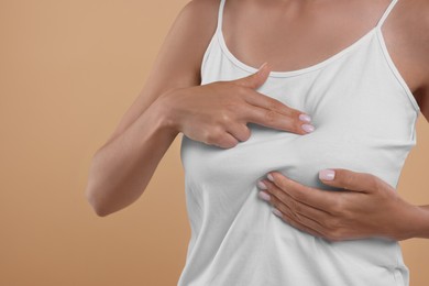 Woman doing breast self-examination on light brown background, closeup. Space for text