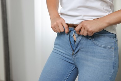 Photo of Woman trying to put on tight jeans indoors, closeup. Space for text