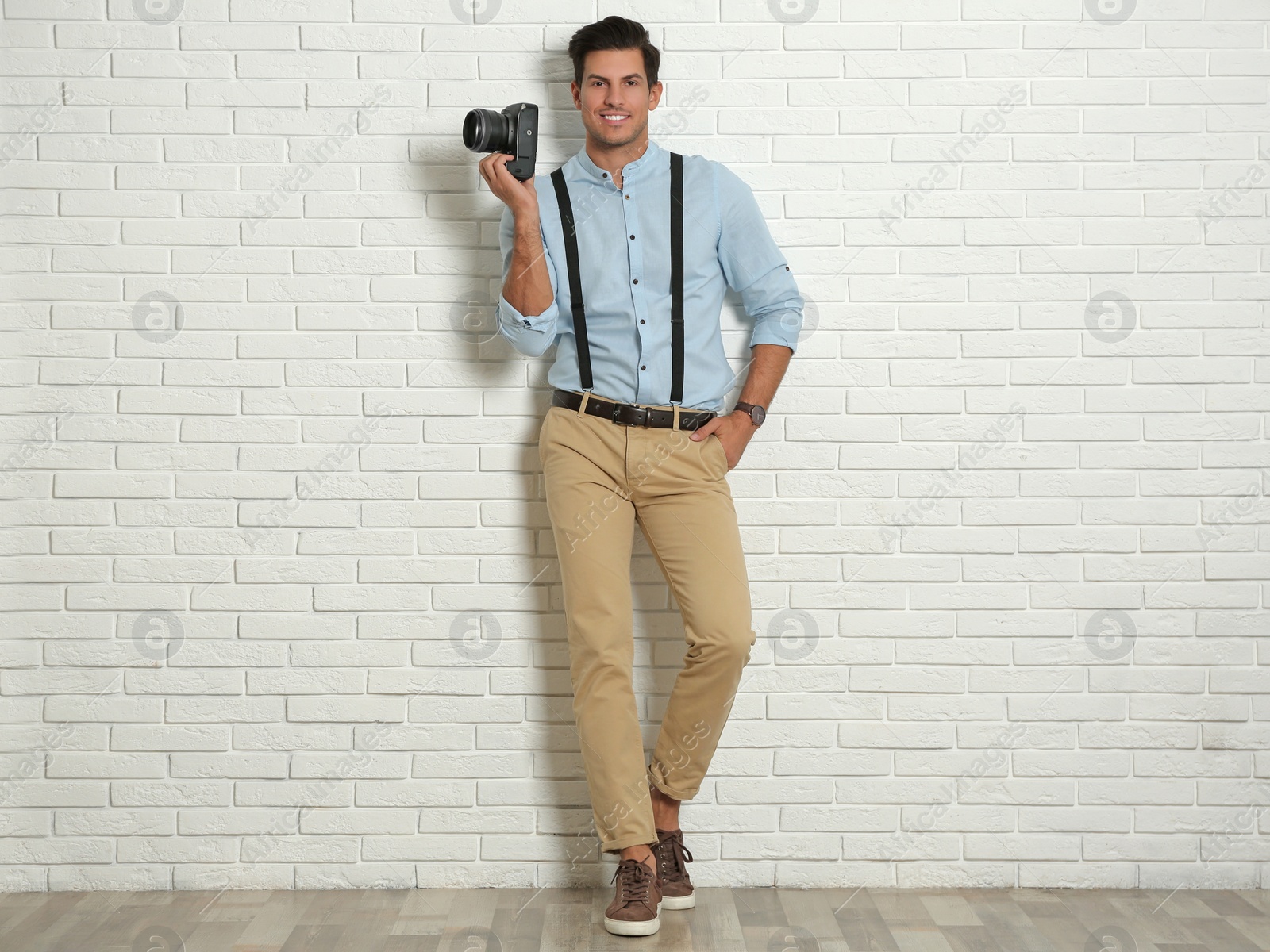 Photo of Professional photographer working near white brick wall in studio. Space for text