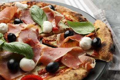 Photo of Tasty pizza with cured ham, olives, mozzarella cheese, sun-dried tomato and basil on table, closeup