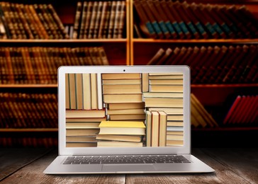 Online library. Modern laptop on wooden table and shelves with books indoors