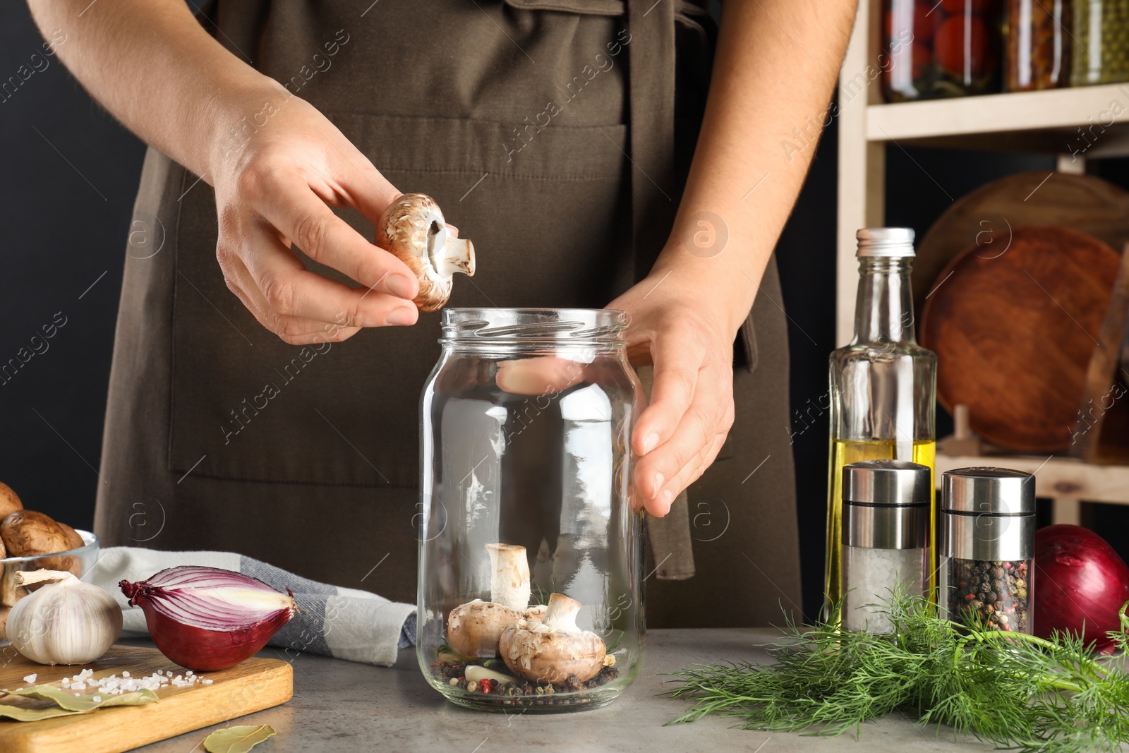 Photo of Woman putting mushroom into jar at light grey table, closeup