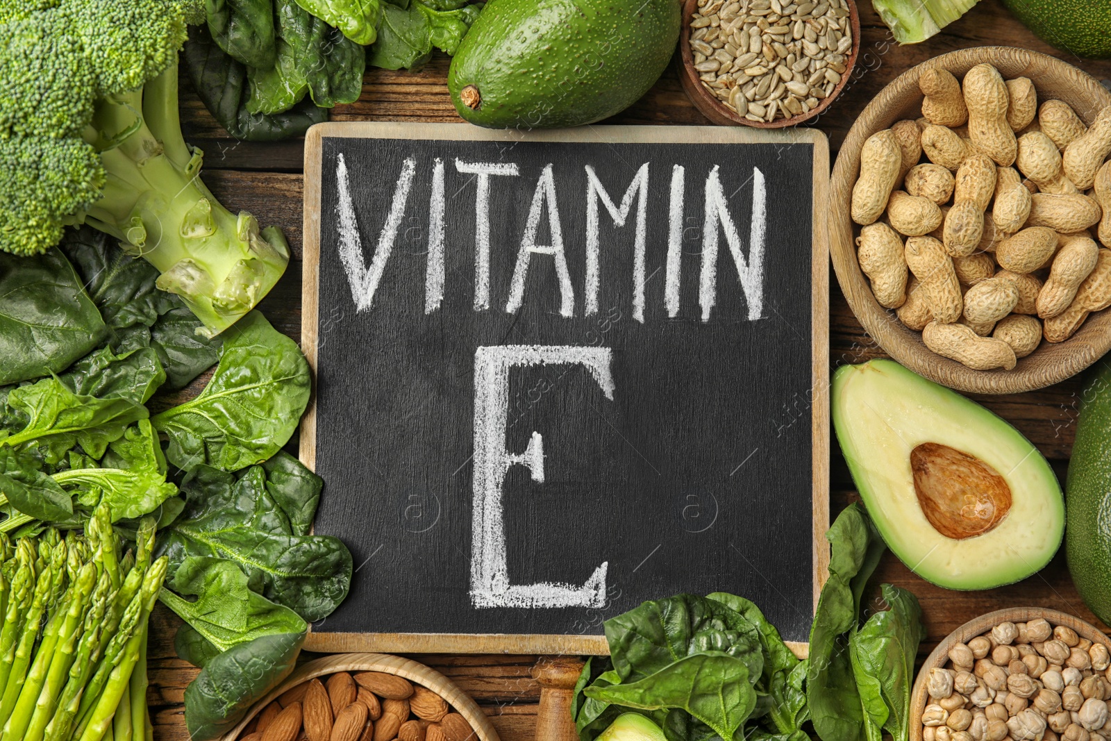 Photo of Small chalkboard with phrase Vitamin E and different products on wooden table, flat lay