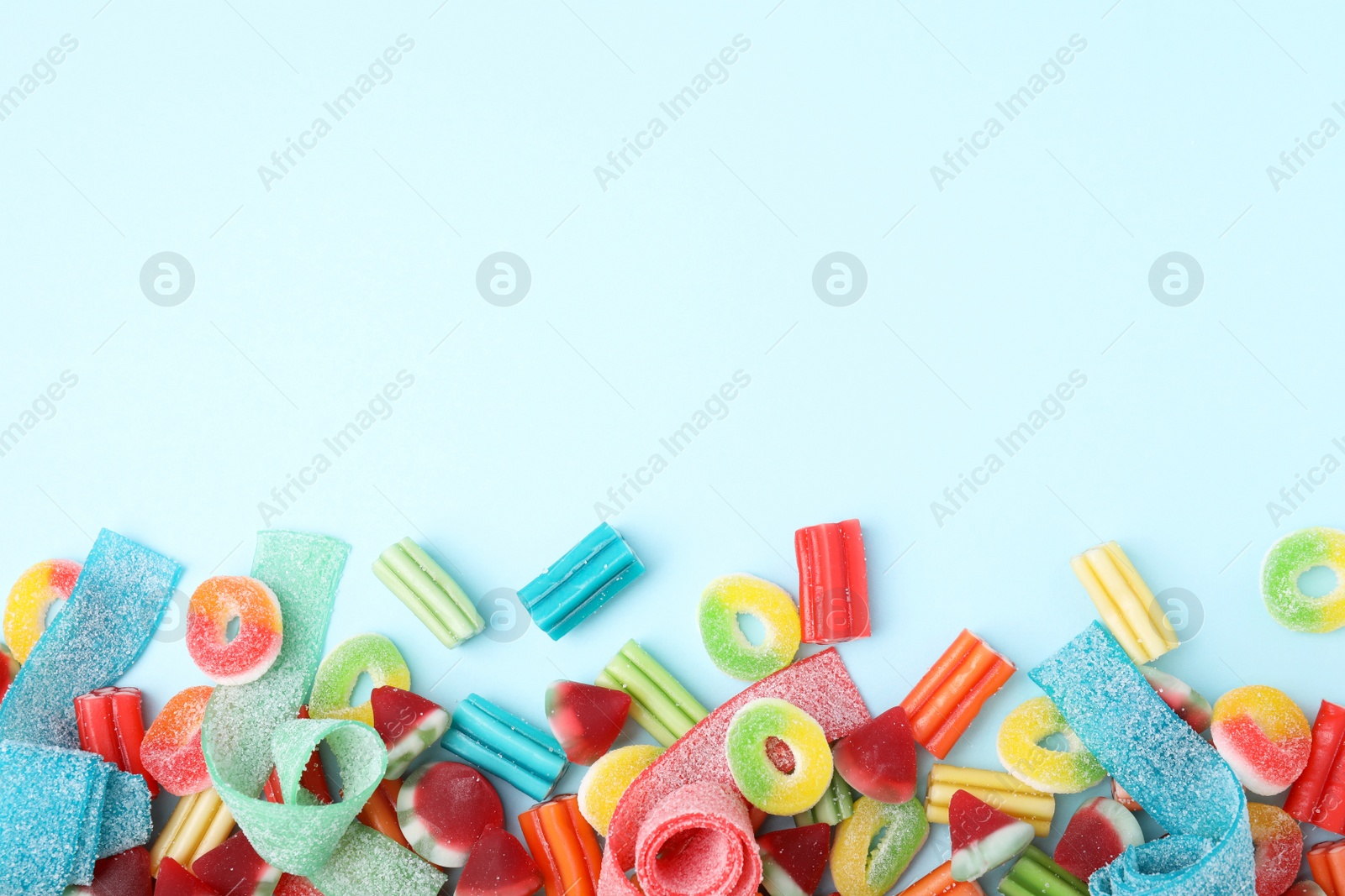 Photo of Many different jelly candies on light blue background, flat lay. Space for text