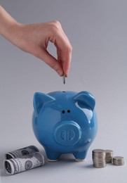 Financial savings. Woman putting coin into piggy bank on grey background, closeup