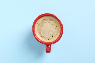 Tasty coffee in cup on light blue background, top view