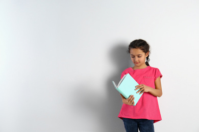 Photo of Cute little girl with book on light background,  space for text