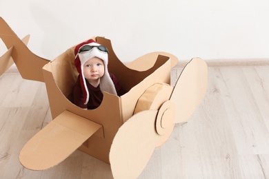 Photo of Adorable little child playing with cardboard plane indoors