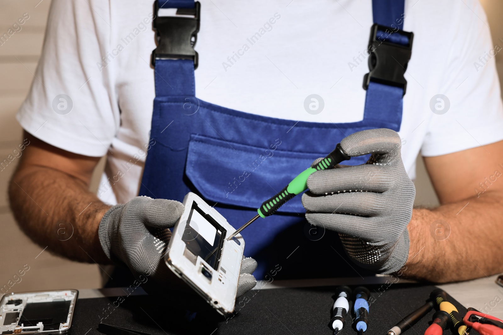 Photo of Technician repairing broken smartphone at table, closeup