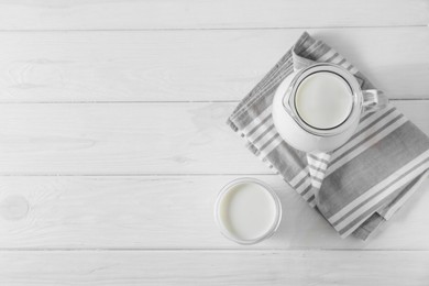Photo of Jug and glass of fresh milk on white wooden table, flat lay. Space for text