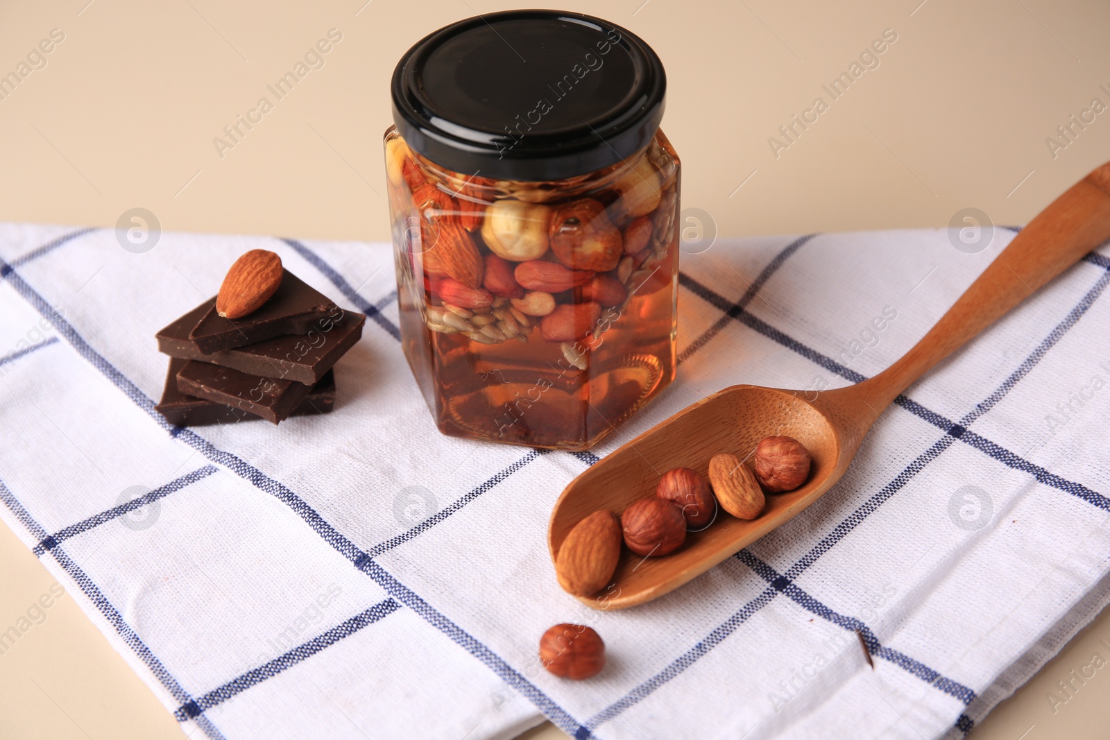 Photo of Different nuts with honey in jar, spoon and chocolate on beige table