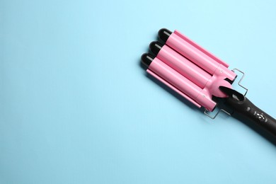 Photo of Modern triple curling hair iron on light blue background, top view. Space for text