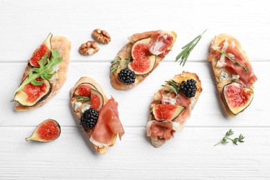 Photo of Sandwiches with ripe figs and prosciutto served on white wooden table, flat lay
