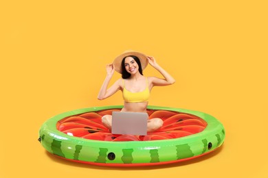 Happy young woman with beautiful suntan and hat using laptop on inflatable mattress against orange background