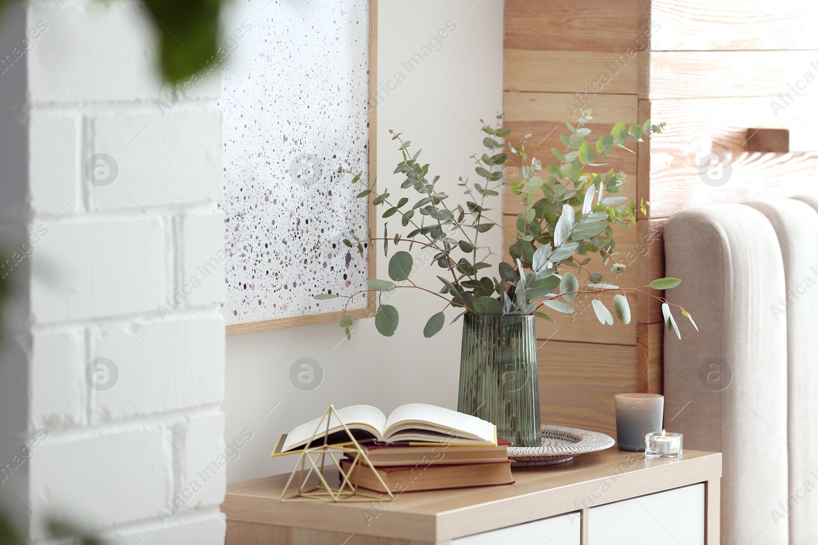 Photo of Beautiful eucalyptus branches and books on cabinet in modern room. Interior design