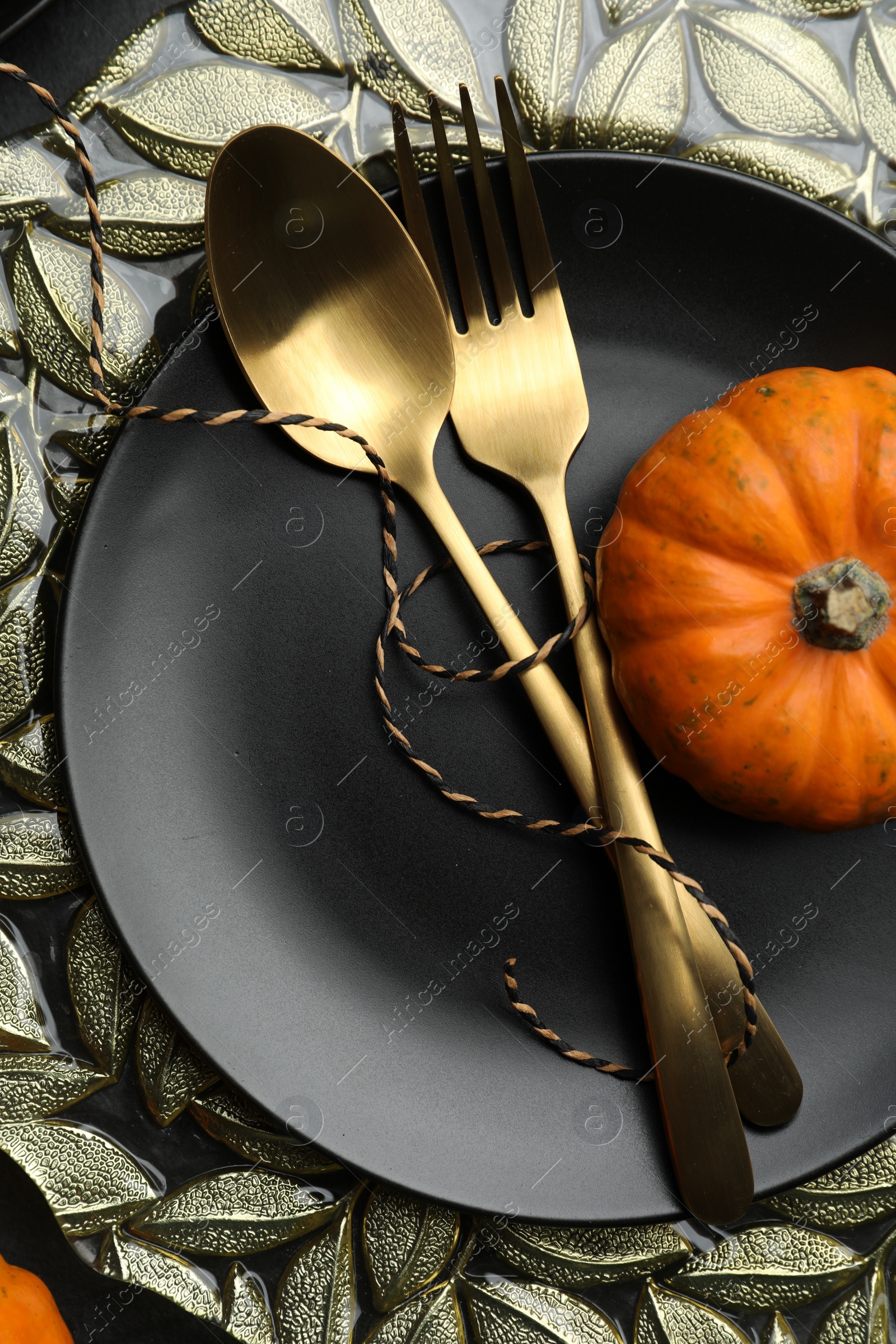 Photo of Autumn table setting with golden cutlery and pumpkin on black background, closeup