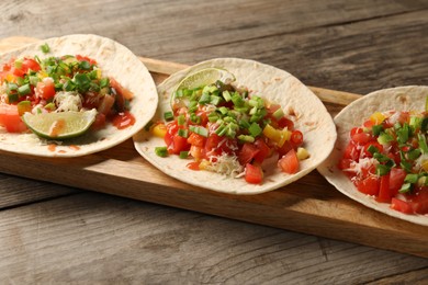 Photo of Delicious tacos with vegetables, green onion, lime and ketchup on wooden table