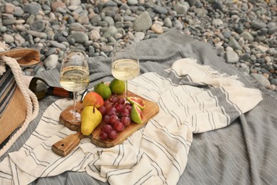Photo of White wine and fresh fruits on picnic blanket outdoors