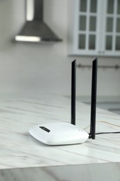 Photo of Modern Wi-Fi router on white marble table in kitchen