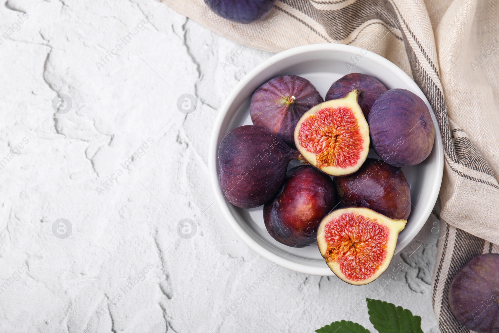 Photo of Bowl of tasty ripe figs on white textured table, flat lay. Space for text