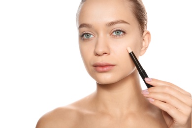 Young woman applying foundation on her face against white background