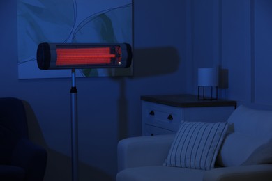 Photo of Electric infrared heater in dark living room at night