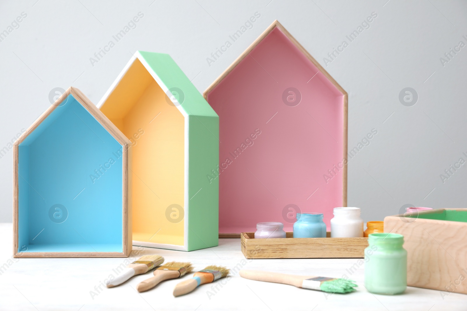 Photo of House shaped shelves, jars of paints and brushes on white table. Interior elements