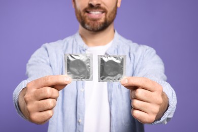 Photo of Man holding condoms on purple background, closeup. Safe sex