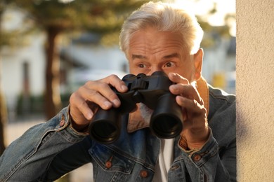 Photo of Concept of private life. Curious senior man with binoculars spying on neighbours outdoors
