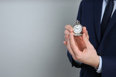 Closeup view of businessman holding pocket watch on grey background, space for text. Time management