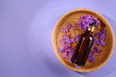 Photo of Bottle with essential oil, lilac flowers and water in bowl on violet background, top view. Space for text