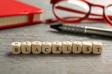 Photo of Cubes with word Blacklist and office stationery on grey wooden desk, closeup
