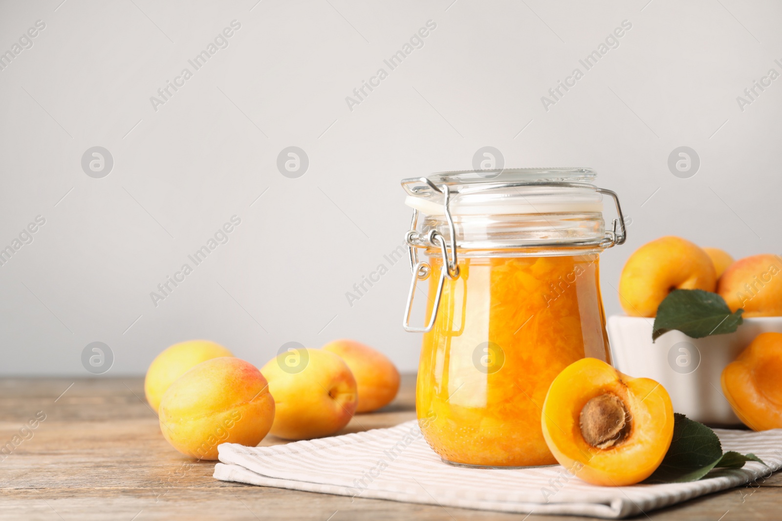 Photo of Jar of apricot jam and fresh fruits on wooden table. Space for text