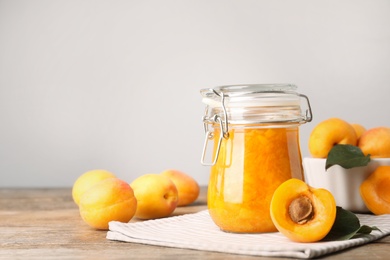 Photo of Jar of apricot jam and fresh fruits on wooden table. Space for text