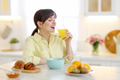 Photo of Smiling woman drinking juice at breakfast indoors