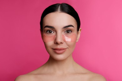 Beautiful young woman with under eye patches on pink background