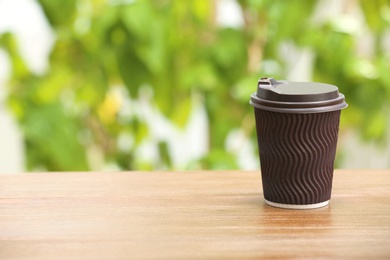 Cardboard cup of coffee on table against blurred background. Space for text