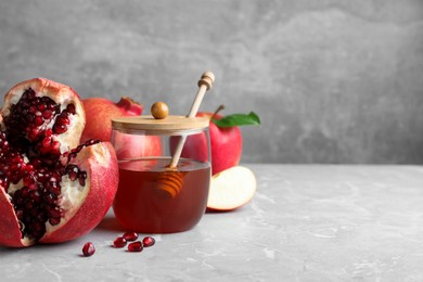 Photo of Honey, pomegranate and apples on grey marble table, space for text. Rosh Hashana holiday
