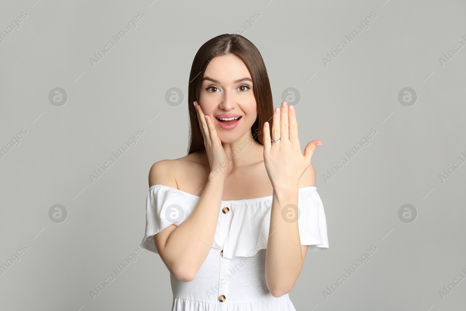 Photo of Happy young woman wearing beautiful engagement ring on grey background