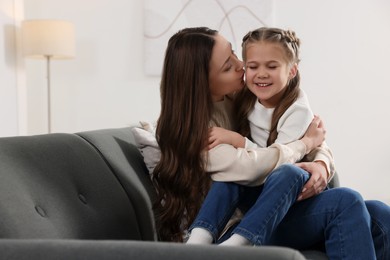 Photo of Happy mother kissing her cute daughter on sofa at home