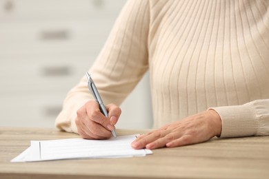 Senior woman signing Last Will and Testament at wooden table indoors, closeup