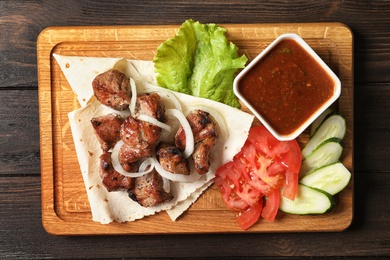 Photo of Wooden board with shish kebab and sauce on table, top view