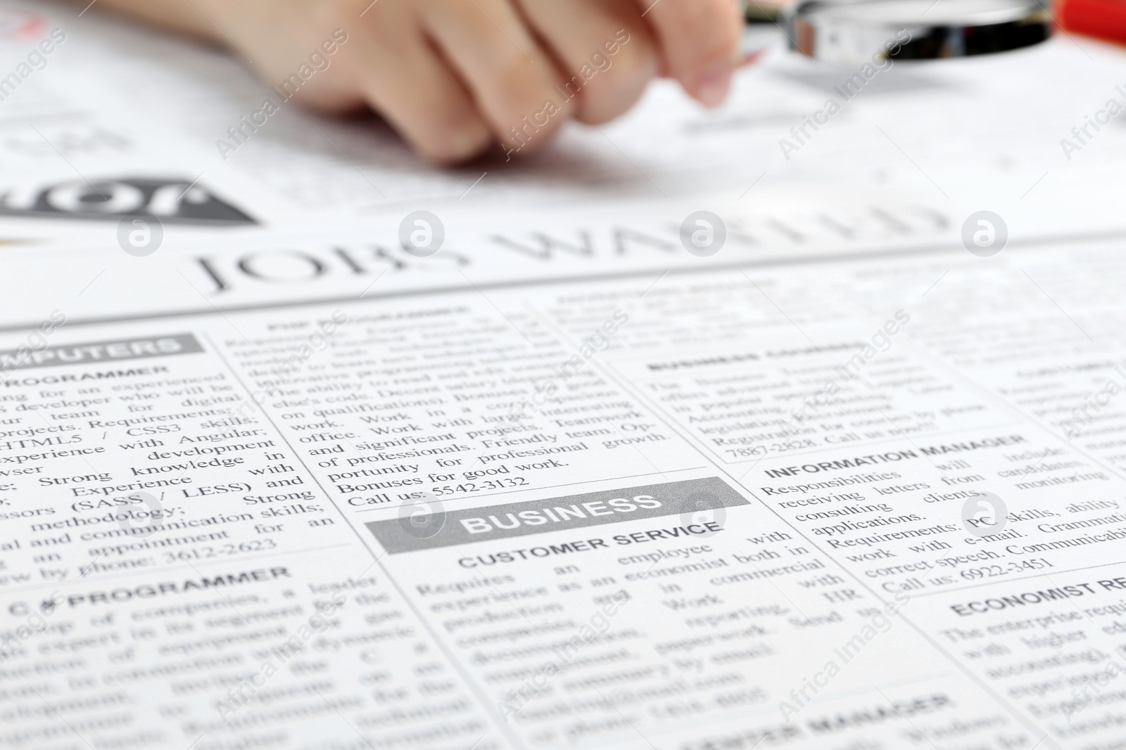 Photo of Woman looking through magnifying glass at newspaper, closeup. Job search concept