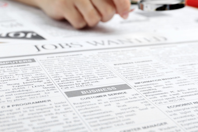 Photo of Woman looking through magnifying glass at newspaper, closeup. Job search concept